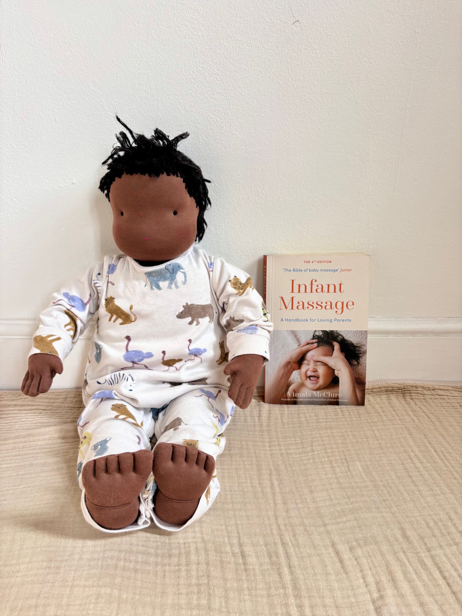 Infant massage teaching doll seated beside an Infant Massage book