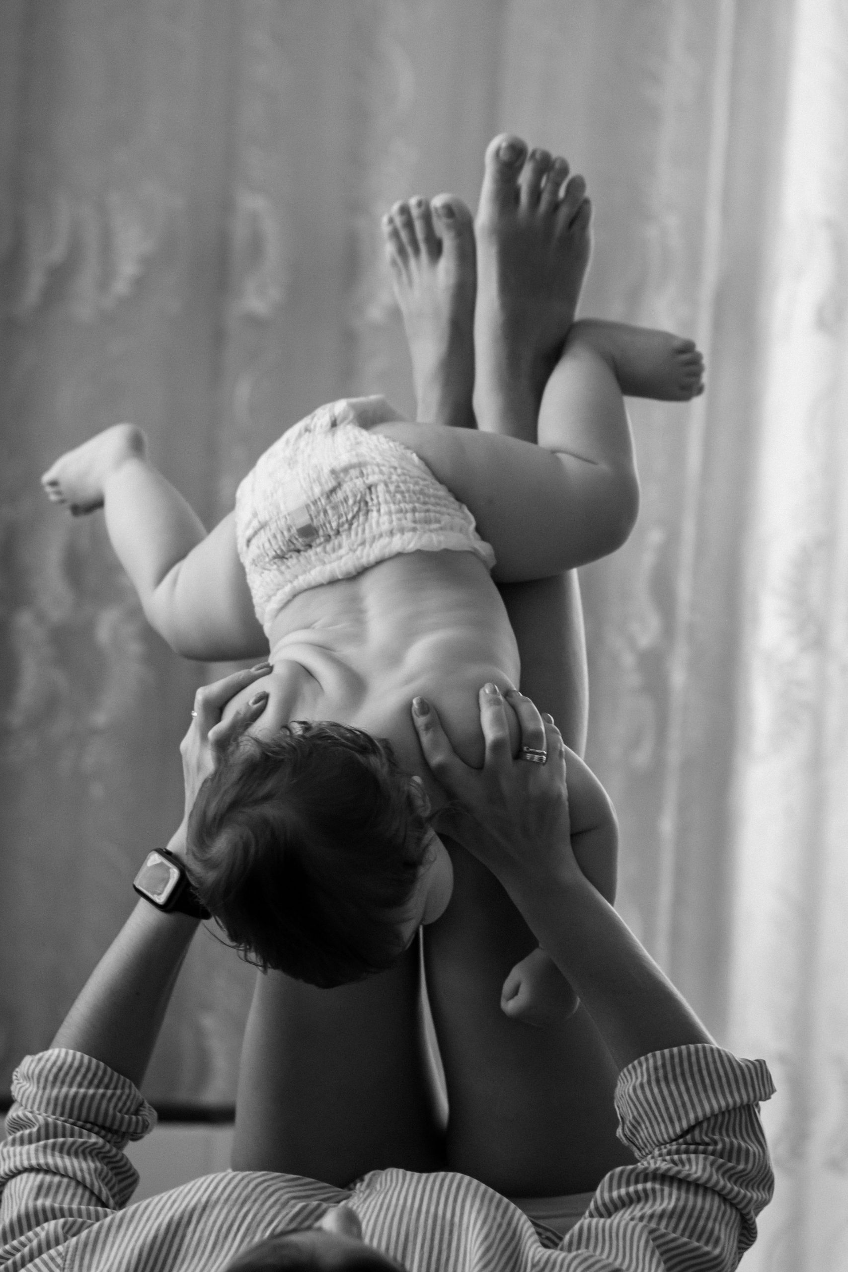 Parent lying down, playfully lifting baby overhead, black and white photo