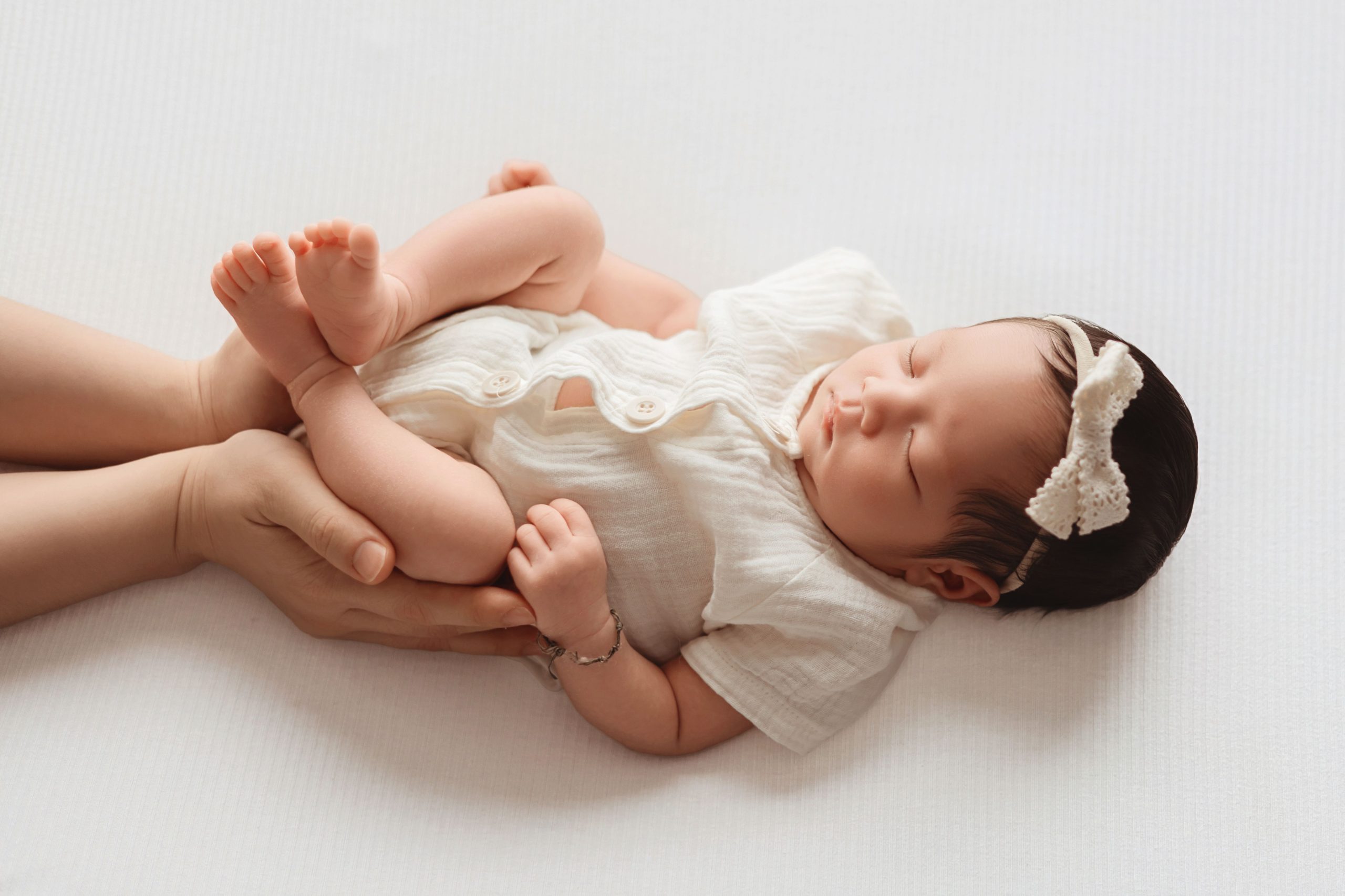Adult hands gently cradling a baby lying down