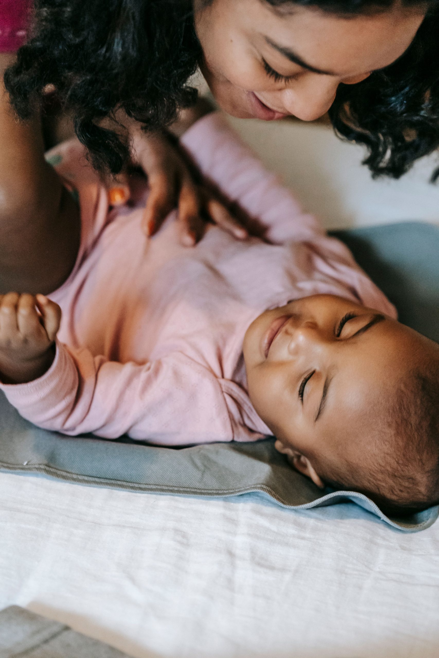 Parent smiling down at baby lying on a bed during touch